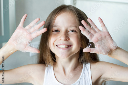 Happy smiling girl washing hands, show hands in soap bubbles to the camera.