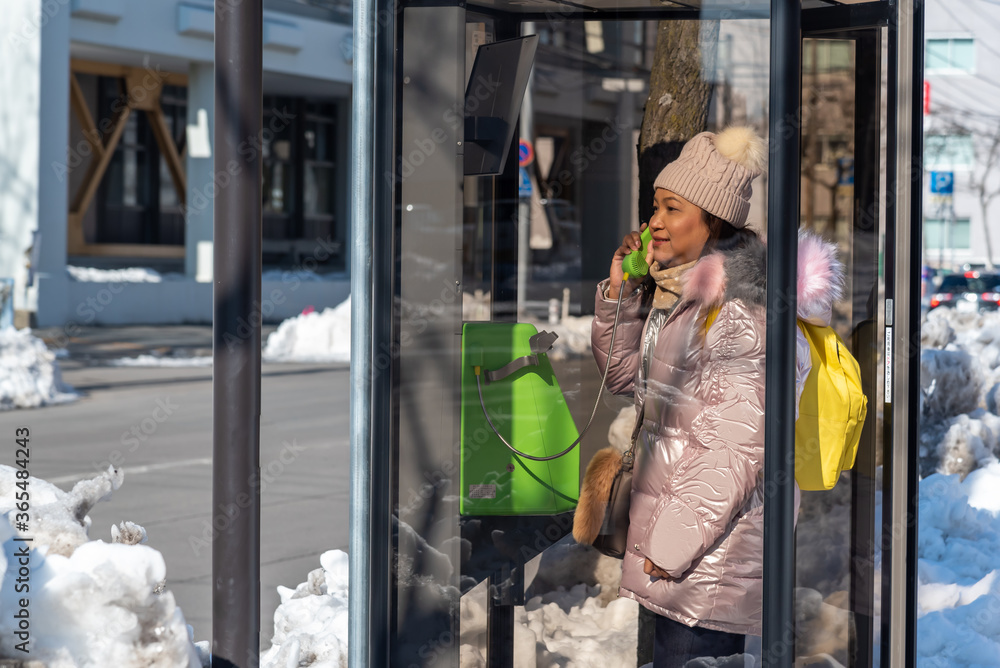 Young Asian woman talking on public phone booth.