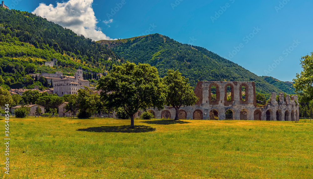 A view across a park towards the remains of the Roman amphitheater in front of the city of Gubbio, Italy in summer