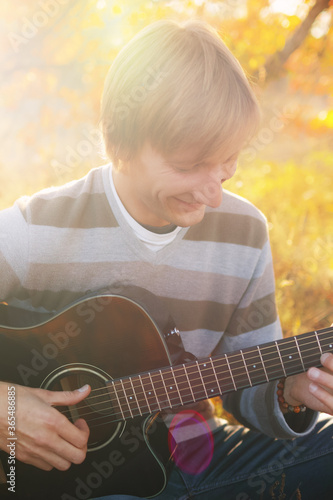 Young caucasian man in a sweater playing an acoustic guitar in the autumn forest.