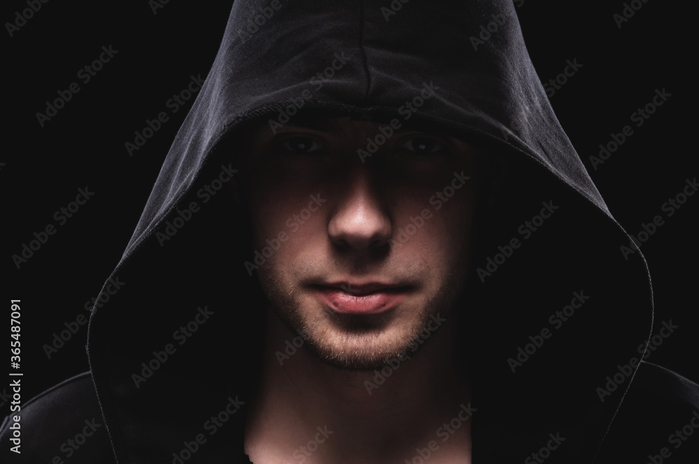 Close-up portrait of a courageous man in a deep dark hood on a black background. The concept of secrecy of secrets and people hiding from the government. Hackers and thieves. Low key Close-up portrait of a courageous man in a deep dark hood on a black background. The concept of secrecy of secrets and people hiding from the government. Hackers and thieves. Low key