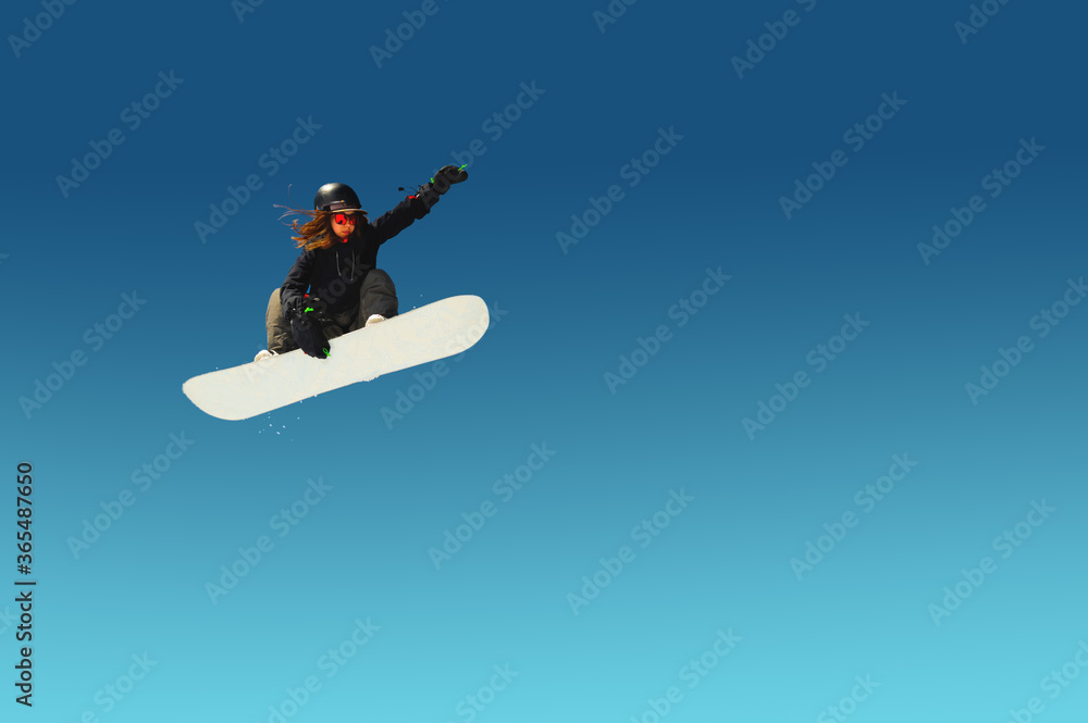 Girl snowboarder in flight after jumping amid blue sky gradient blank designer winter snowboarding sport