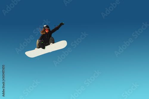 Girl snowboarder in flight after jumping amid blue sky gradient blank designer winter snowboarding sport