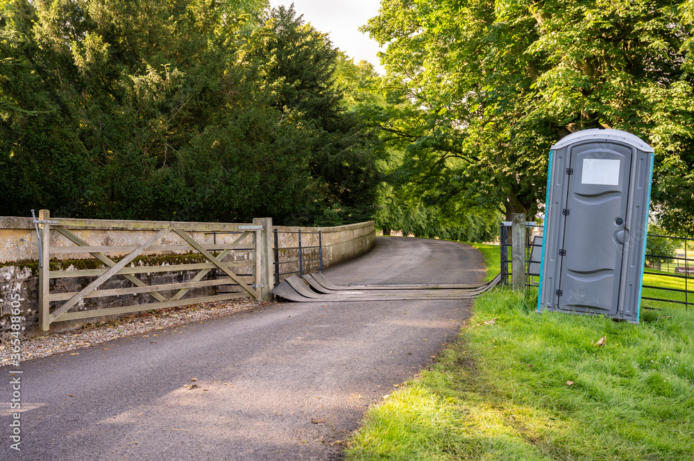 A plastic portable toilet next to a covered cattle grid on a public footpath in a field at an outdoor event A plastic portable toilet next to a covered cattle grid on a public footpath in a field at an outdoor event