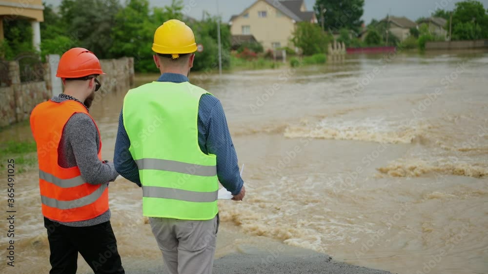 Two male engineers solve flood problem. Devastation wrought after massive disasters. Flooded outskirts of city. Traffic along overflowing with water street. Floods hit town. Heavy rain. Flooding. Two male engineers solve flood problem. Devastation wrought after massive disasters. Flooded outskirts of city. Traffic along overflowing with water street. Floods hit town. Heavy rain. Flooding.
