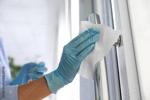 Woman cleaning door handle with wet wipe indoors, closeup photo