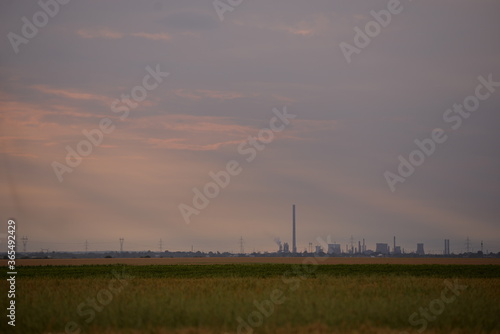 oil refinery seen on the horizon on the wheat field at sunset © badescu