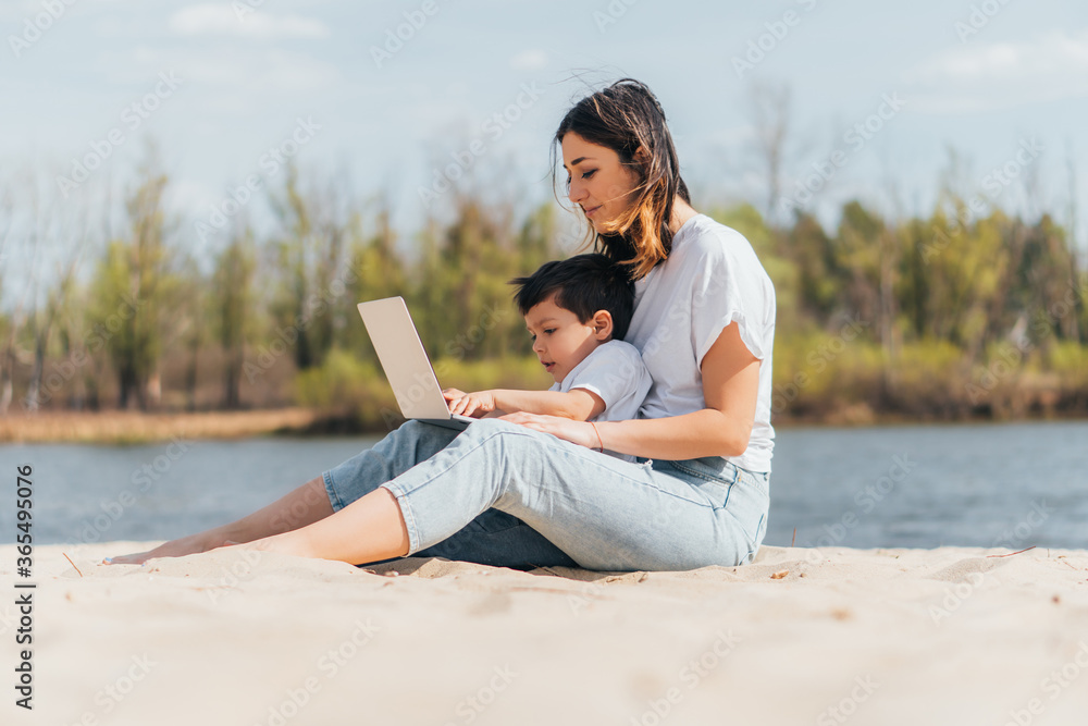 selective focus of mother and son sitting on sand and using laptop