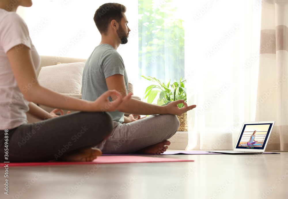 Distance yoga course during coronavirus pandemic. Couple having online practice with instructor via laptop at home - obrazy, fototapety, plakaty 