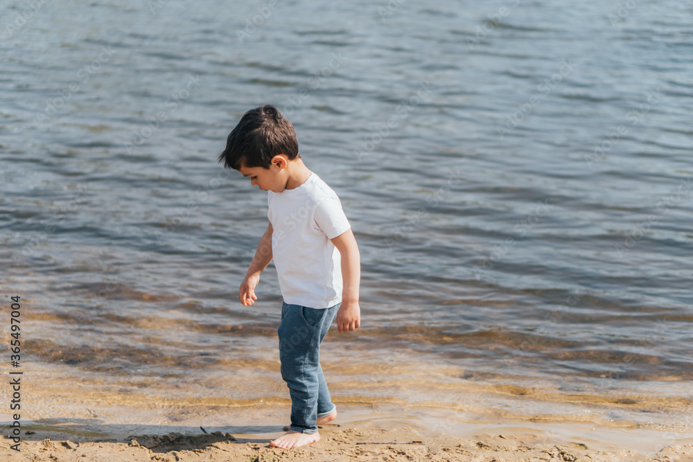 Cute boy in denim jeans standing near blue lake