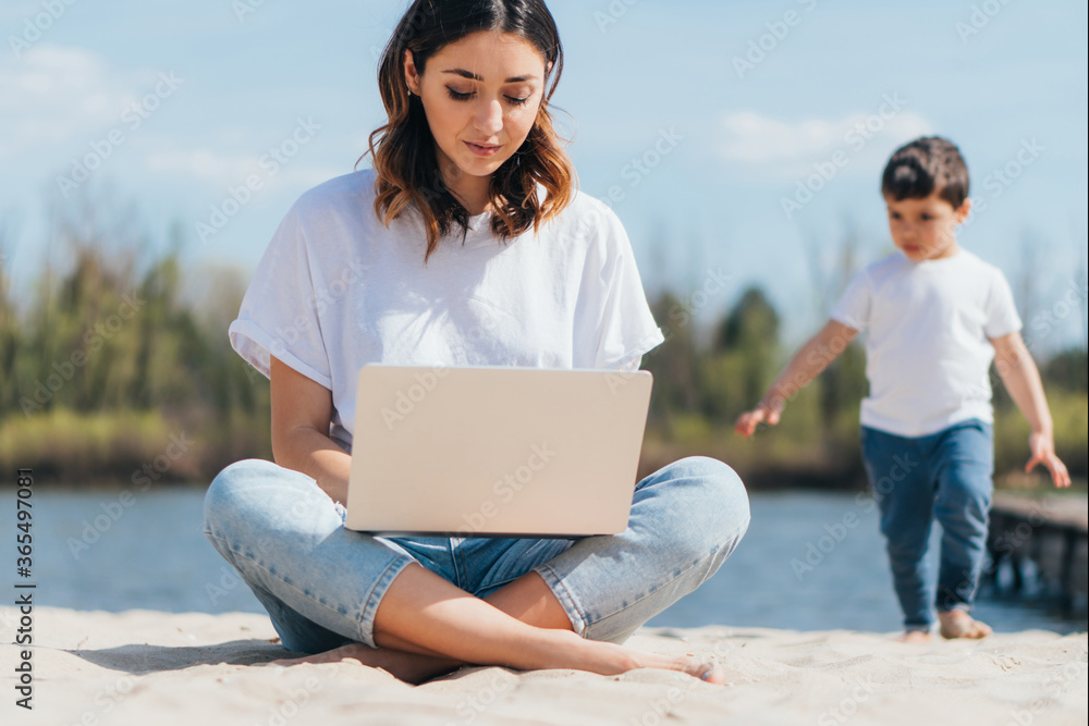 Selective focus of freelancer using laptop while sitting on sand near cute son Selective focus of freelancer using laptop while sitting on sand near cute son