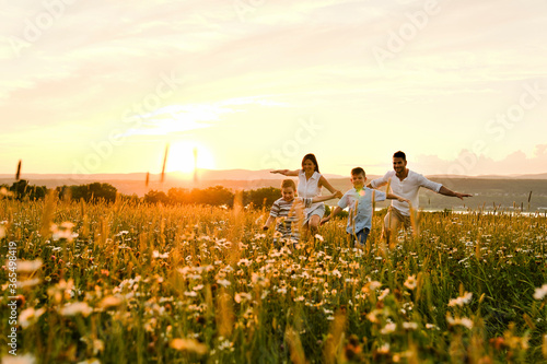 Happy family on daisy field at the sunset having great time together running and fly photo