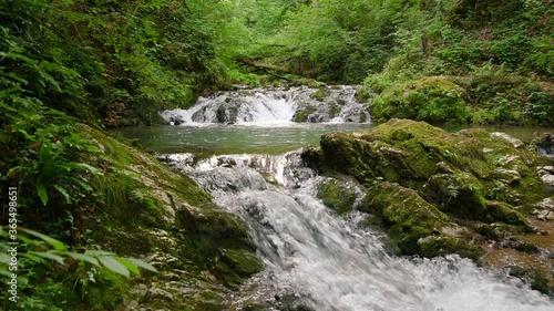 Amazing beautiful nature. Small stream running rapidly in summer green forest. Small natural pool between waterfall cascades. Rocks covered with moss in wilderness. Wide, static shot