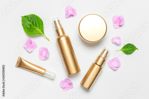 Cosmetic mock up gold bottles. Cosmetics, pink hydrangea flowers on light background. Cosmetics springtime summer Concept. Flat lay top view copy space. Branding products, spa, beauty background