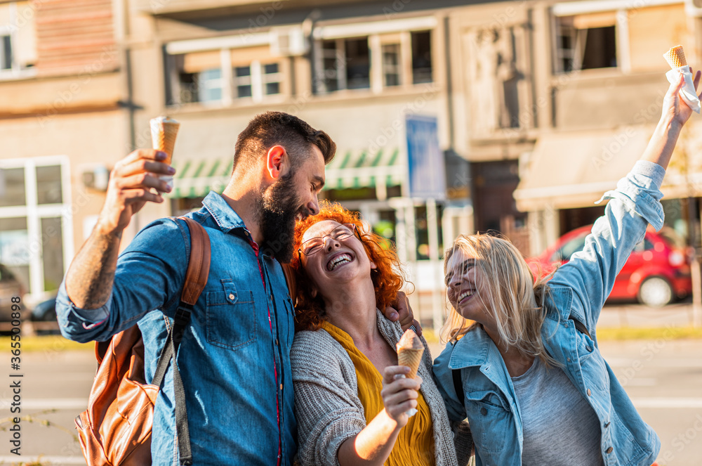 Group of tourists enjoying on vacation, young friends having fun walking on city street eating ice cream during the day.