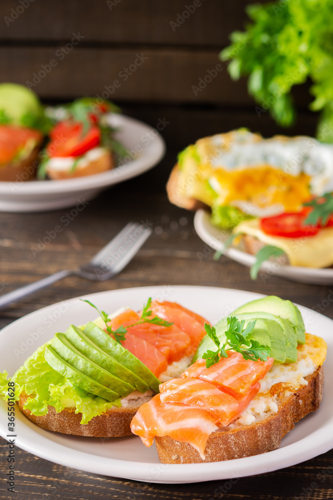 Different delicious sandwiches for breakfast, bread with cheese, avocado and trout, sandwich with egg, tomato and rucola, parsley Different delicious sandwiches for breakfast, bread with cheese, avocado and trout, sandwich with egg, tomato and rucola, parsley