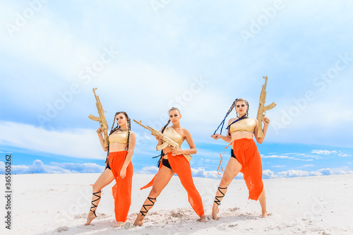 Girls dancers in red skirts and with golden machines in their hands on the beach. White sand and blue sky.