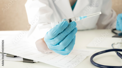 Senior doctor in blue gloves holds a medical syringe for injection isolated over grey background. Dentist, care.