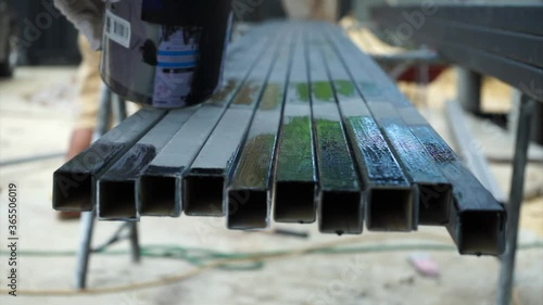 Hands of worker painting the black colour by paintbrush on the surface of steel bars at the construction site