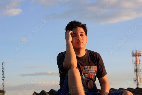 20-year-old male model sitting on the roof adjusting his hair by the wind © Ekkian
