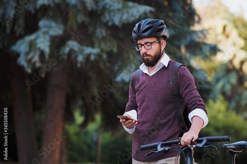 Millennial bike commuter in helmet walks with a phone. Safe cycling in the city, green transport, using bicycle to get around the town