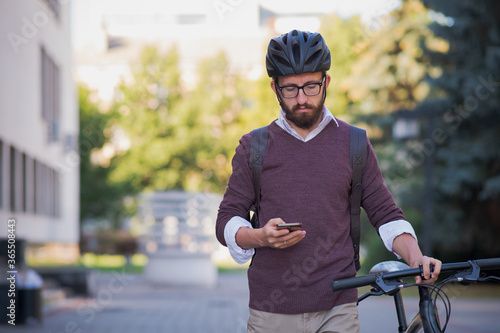 Millennial bike commuter in helmet walks with a phone. Safe cycling in the city, green transport, using bicycle to get around the town