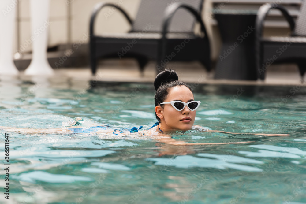 attractive young woman in sunglasses swimming in pool
