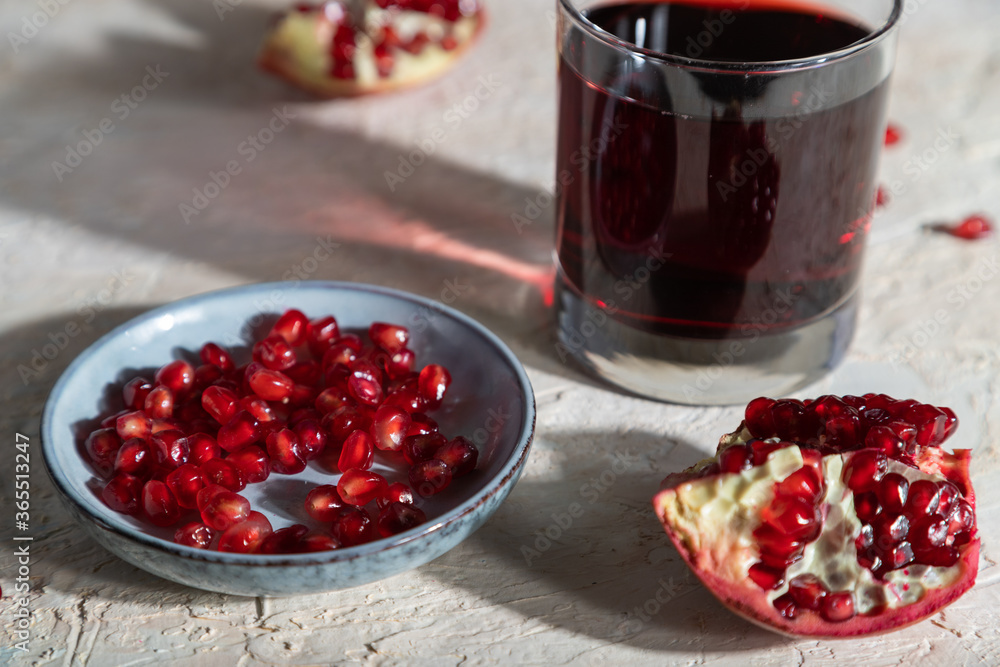 Glass of pomegranate juice on a white concrete background. Hard light, side view, selective focus. Glass of pomegranate juice on a white concrete background. Hard light, side view, selective focus.