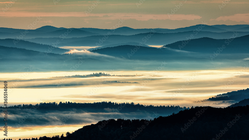 A hazy sunrise in the mountains. Mountains silhouettes and fog in the valleys. Photo from Polonina Wetlinska. Bieszczady National Park. Carpathians. Poland.