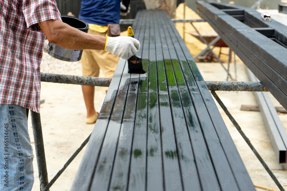 Workers painting the black color by paintbrush on the steel bar at the construction site