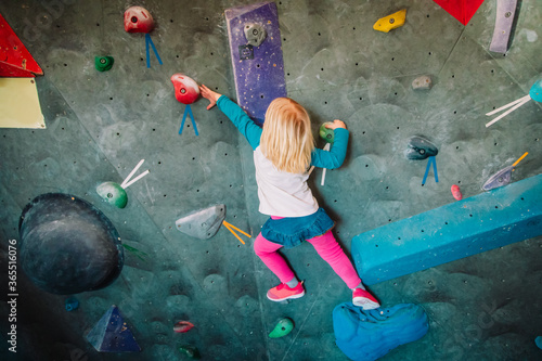 Little girl climbing on artificial boulders wall in gym