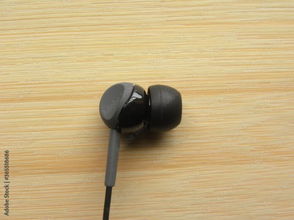 Black color in-ear headphone on wooden table Black color in-ear headphone on wooden table