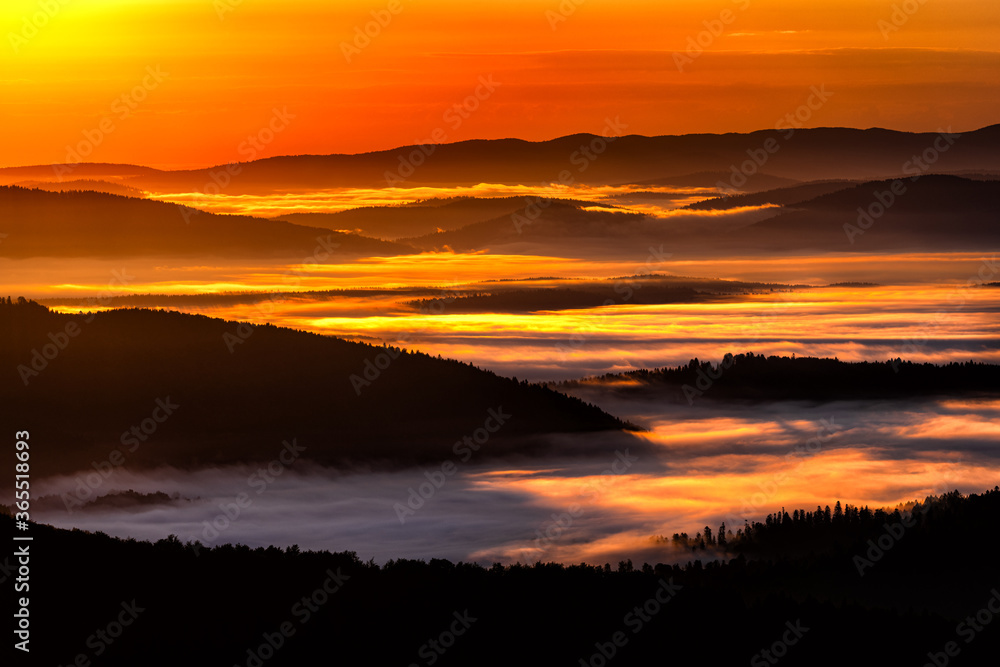 A hazy sunrise in the mountains. Mountains silhouettes and fog in the valleys. Photo from Polonina Wetlinska. Bieszczady National Park. Carpathians. Poland.