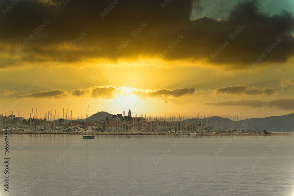 Small dalmatian town of Biograd na Moru, seen from the distance from a nearby hill. Moment of the sun setting in late afternoon, golden illuminated sky, church belltower in the distance