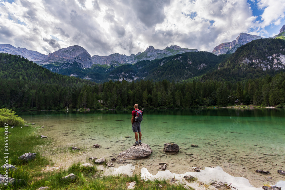 Hiker wearing a backpack enjoying the view from a rock at Tovel Lake in South Tyrol, Italy