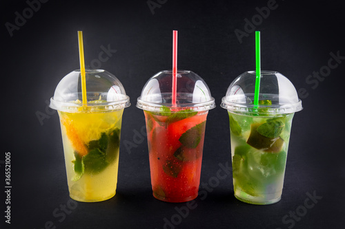 Refreshing summer drink. Colored lemonades,mojito, strawberry in plastic cups with ice on black background. Take away drinks. 