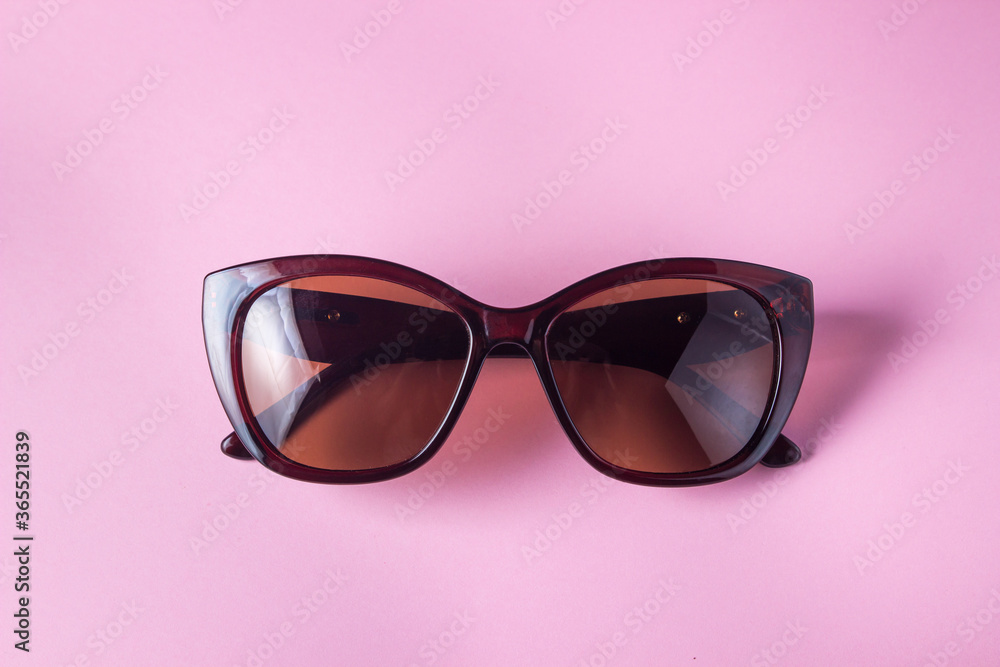 Female glasses on a pink background. Brown sunglasses for women lie on a pink surface. Female glamor Female glasses on a pink background. Brown sunglasses for women lie on a pink surface. Female glamor