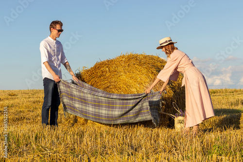 Couple in love preparing for a picnic in field. Young man and young woman in a pink dress spreading a plaid. photo