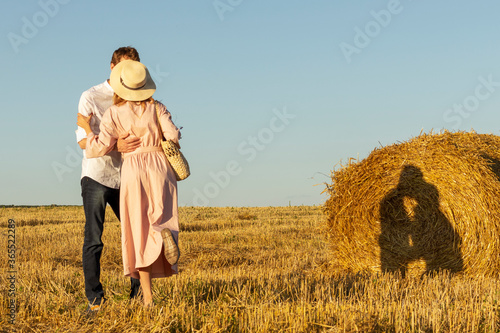 Couple in love kissing in a wheat field. Shadow of this young people falls on a hay bale.