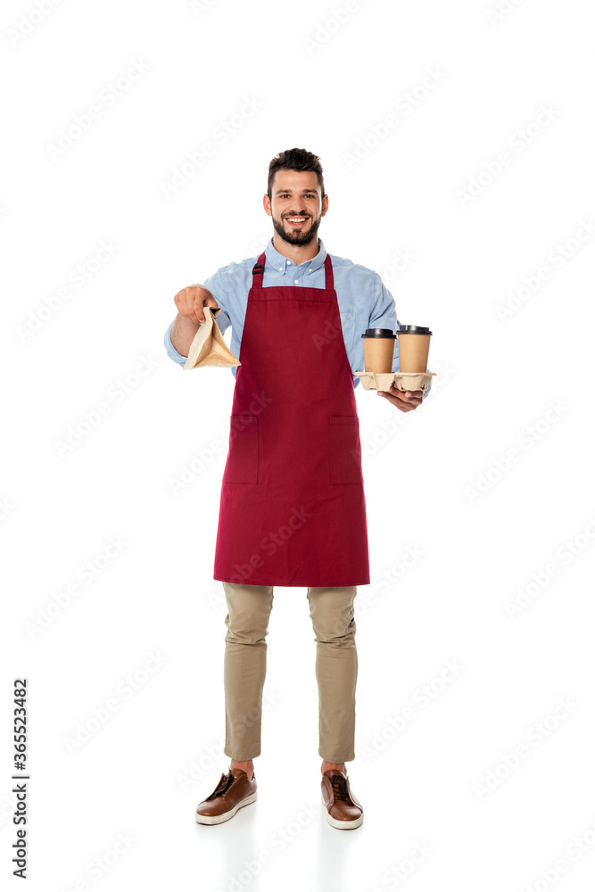 Handsome positive waiter holding paper bag and disposable cups on white background Handsome positive waiter holding paper bag and disposable cups on white background