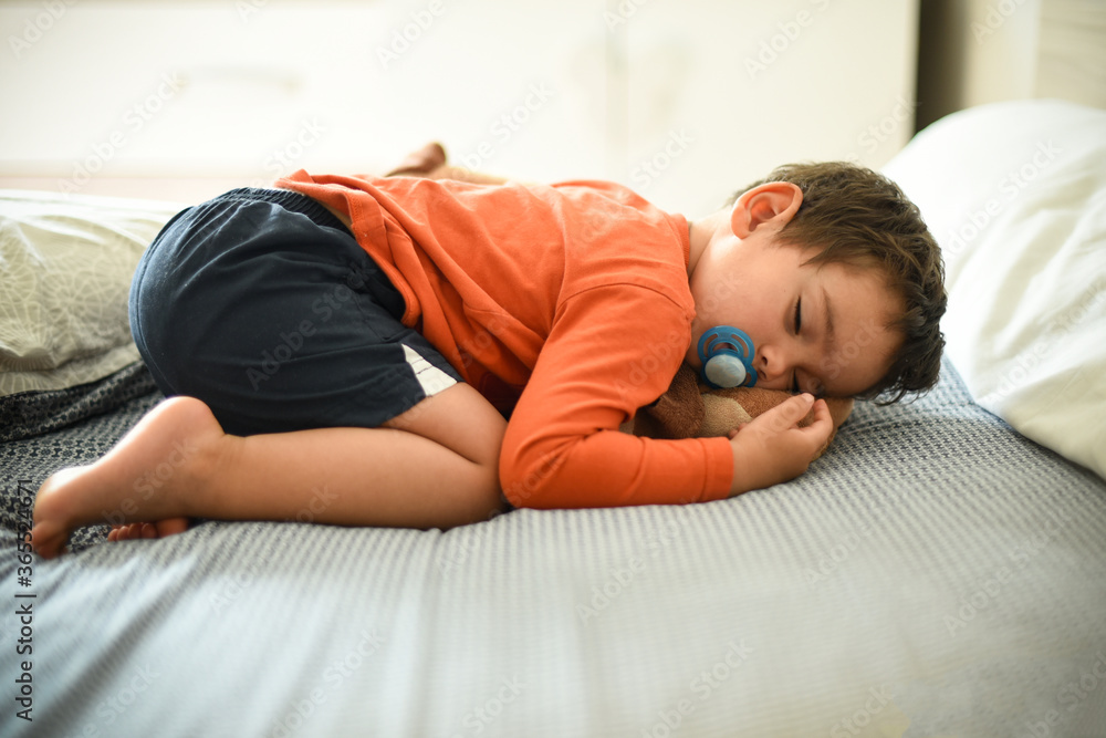 young child sleeping on a bed with his plush