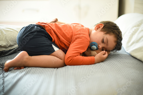 young child sleeping on a bed with his plush