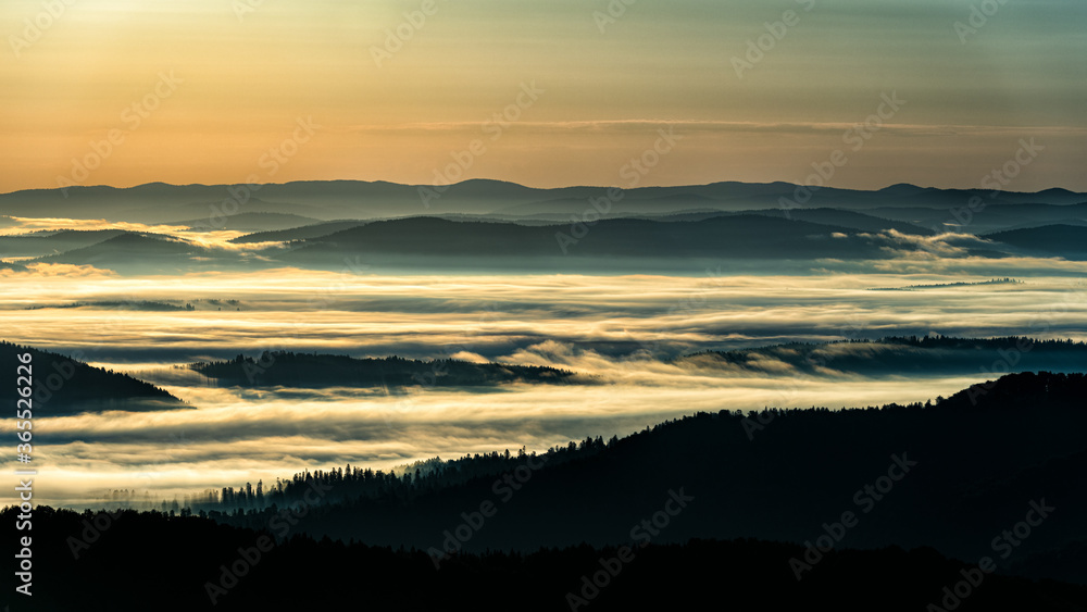 Fototapeta premium A hazy sunrise in the mountains. Mountains silhouettes and fog in the valleys. Photo from Polonina Wetlinska. Bieszczady National Park. Carpathians. Poland.