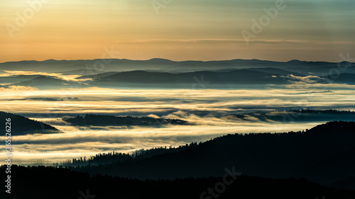 Fototapeta Naklejka Na Ścianę i Meble -  A hazy sunrise in the mountains. Mountains silhouettes and fog in the valleys. Photo from Polonina Wetlinska. Bieszczady National Park. Carpathians. Poland.
