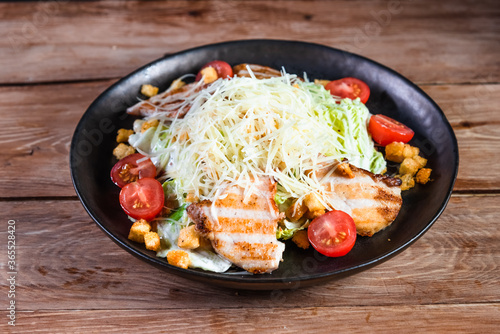 Appetizing Caesar salad with chicken in a black plate on a wooden table. The concept of healthy food and serving