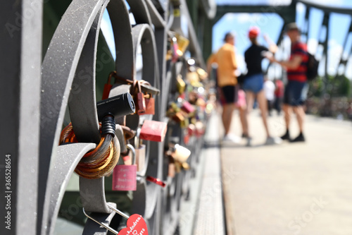 Close up of heart shaped love padlocks at bridge called 'Eiserner Steg' in Frankfurt city with blurry tourists in background