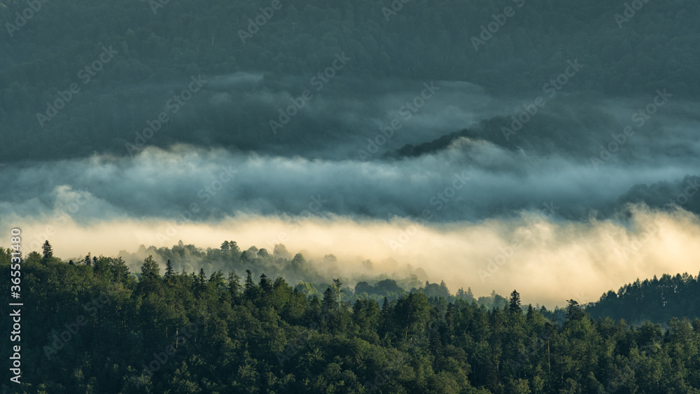 A hazy sunrise in the mountains. Mountains silhouettes and fog in the valleys. Photo from Polonina Wetlinska. Bieszczady National Park. Carpathians. Poland. A hazy sunrise in the mountains. Mountains silhouettes and fog in the valleys. Photo from Polonina Wetlinska. Bieszczady National Park. Carpathians. Poland.