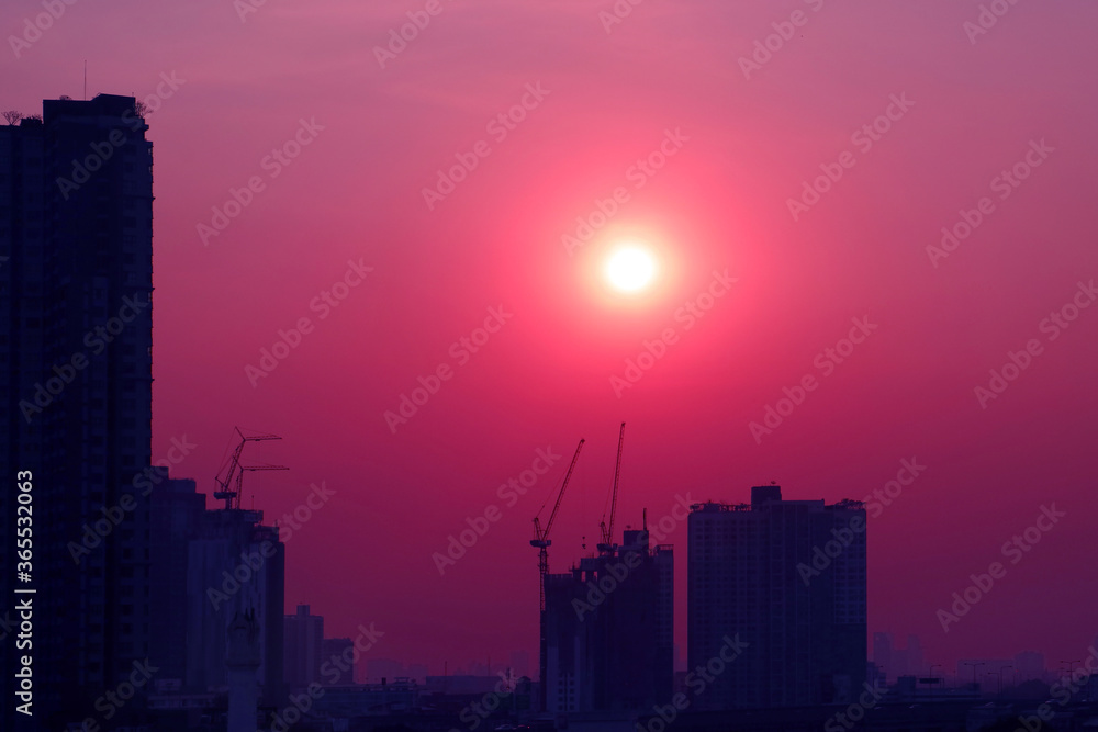 Pop art style purple pink colored sky with dazzling sun rising over the silhouette of construction site	