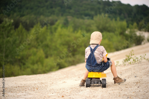 Child, little boy have fun with toy excavator and dumper in the sand. Carefree childhood.