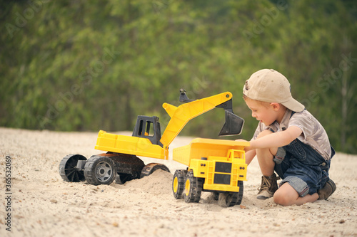 Child, little boy have fun with toy excavator and dumper in the sand. Carefree childhood.